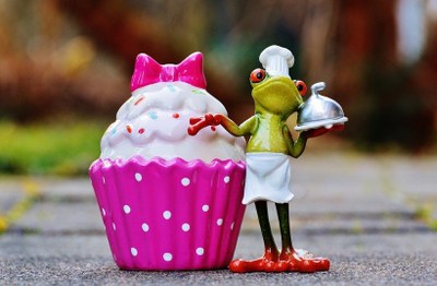 Frog chef standing next to huge pink cupcake
