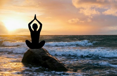 Shadowed person doing yoga posein front of sunrise over crashing waves  o