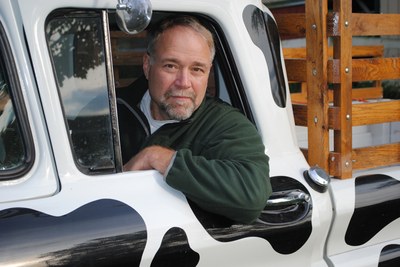 man leaning out the window of a truck painted to look like a cow